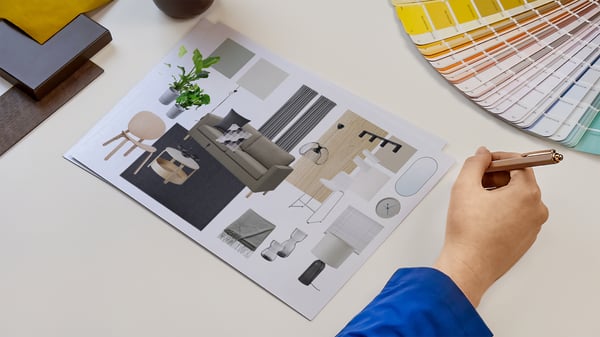 Projektantka wnętrz IKEA prezentująca kartki z wydrukiem kolażu produktowego zaprojektowanego pomieszczenia. Obok na blacie leży wzornik kolorów i próbki materiałów.
