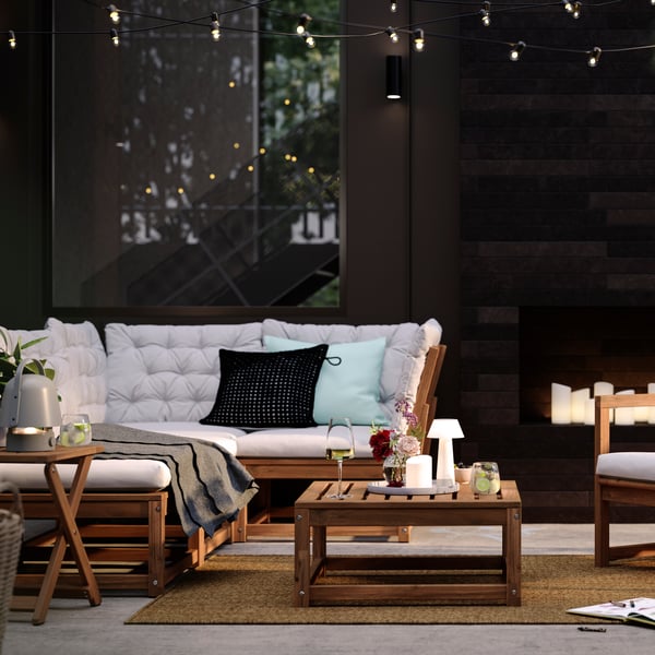 A patio with light brown stained outdoor NÄMMARÖ lounge seating and a seat section for a modular sofa doubling as a table.