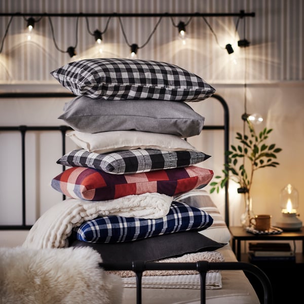 A big pile of pillows on top of the STJÄRNÖ bed, all in warm colours such as dark blue, dark red and warm beige.