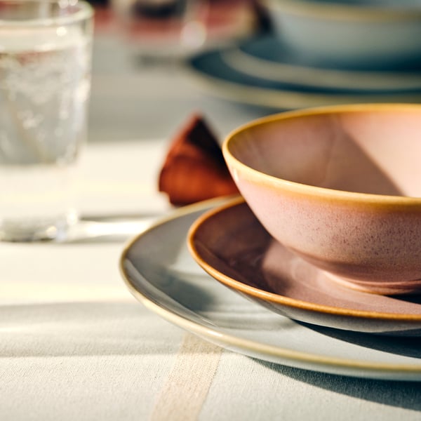 Une table composée de bols et d'assiettes FÄRGLAR empilés les uns sur les autres, et d'un verre derrière, le tout sur un tapis de table.