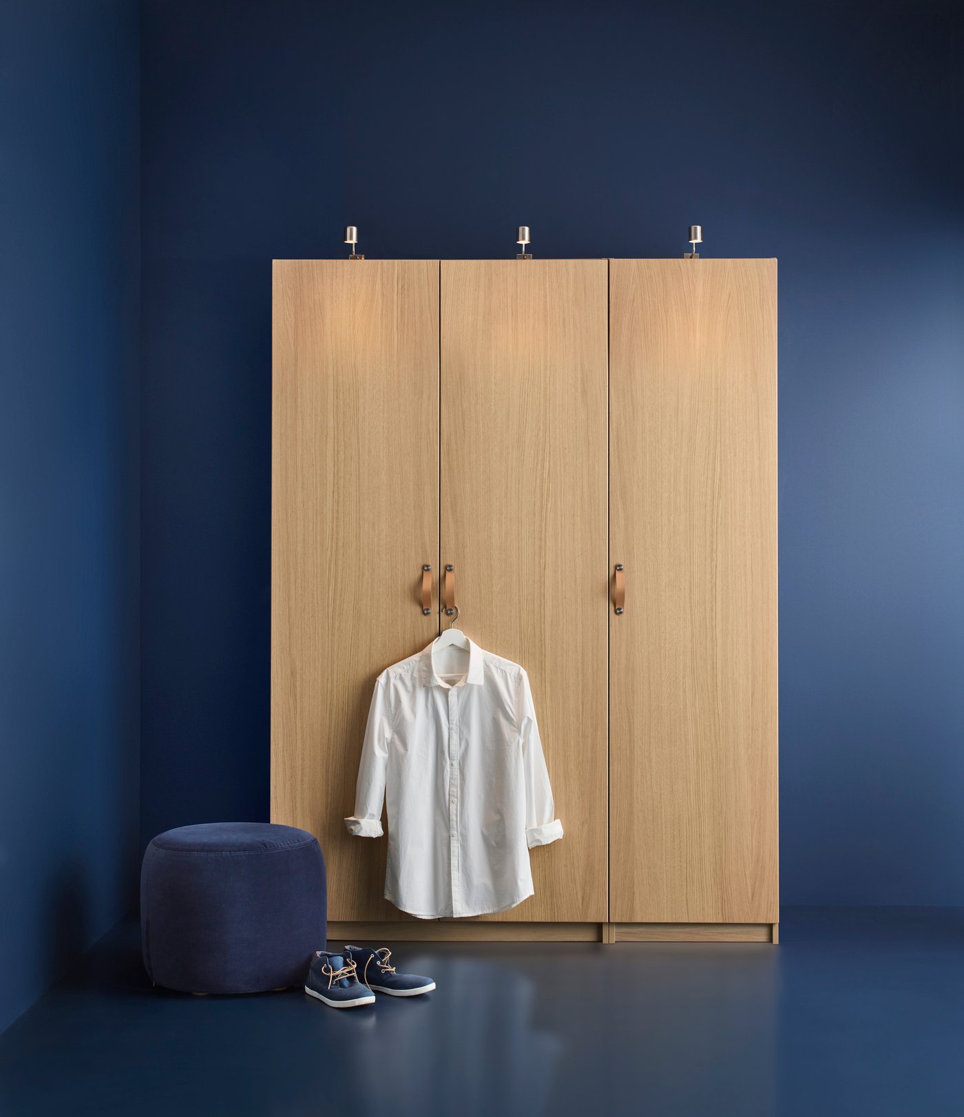 Ein PAX Kleiderschrank in einem blau gestrichenen Raum. An einem Kleiderbügel hängt ein weisses Hemd am Türknopf. Auf dem Boden steht ein Paar Schuhe.