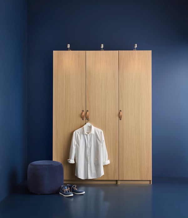 A PAX wardrobe in a blue room with a coat hanger on the door knob holding a white shirt and a pair of shoes on the floor.