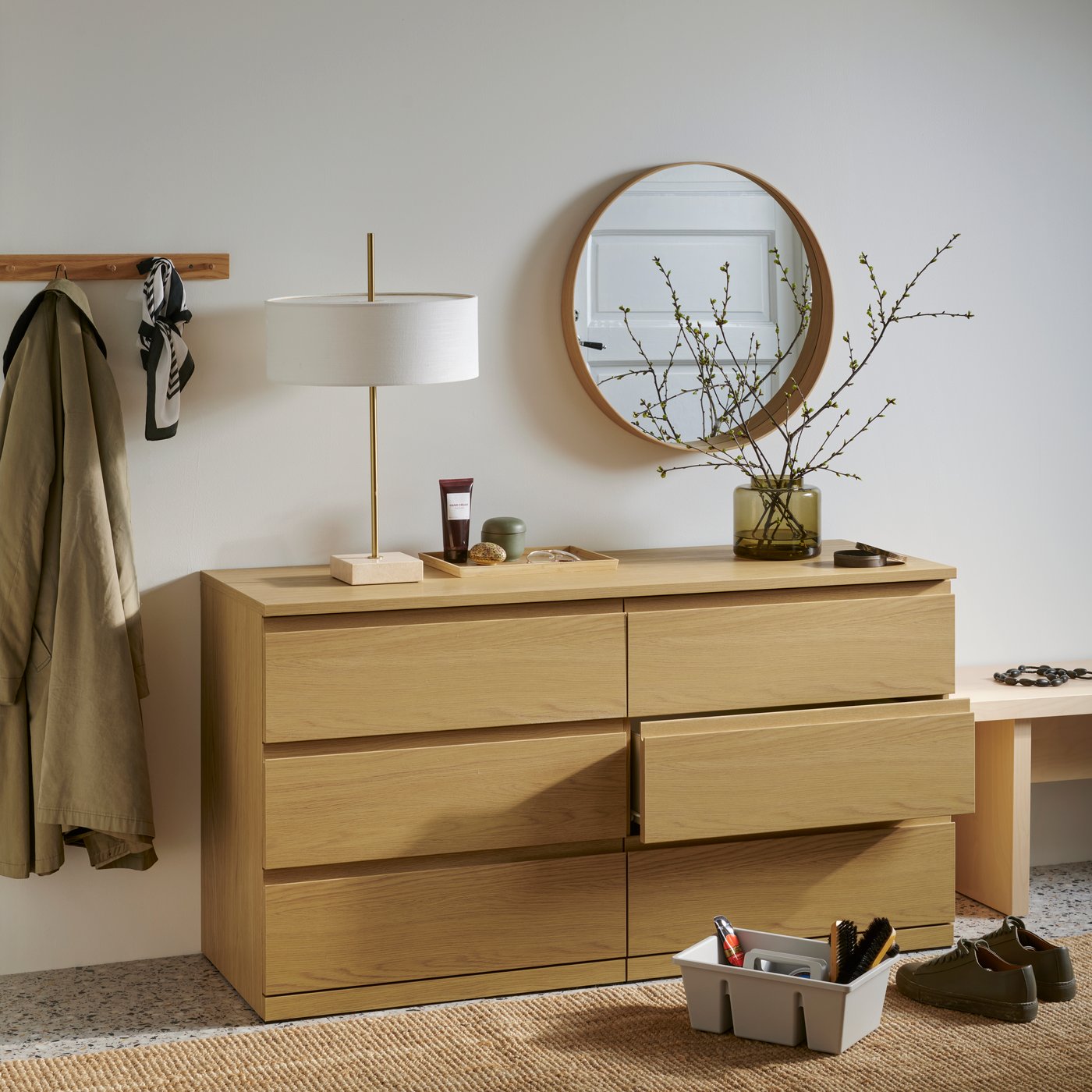 En STORKLINTA byrå med sex lådor i ekeffekt, med en lampa och andra föremål ovanpå samt skovårdsartiklar på golvet.