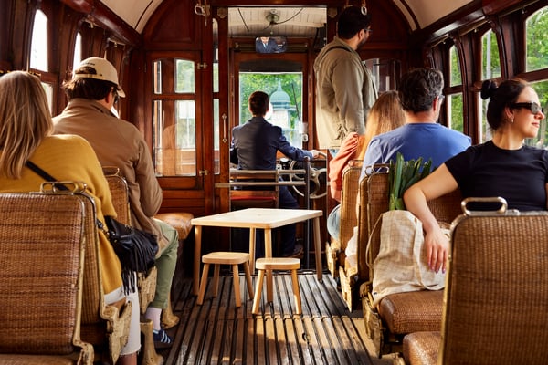 Two FLISAT stools and a FLISAT table rides a tram surrounded by people.