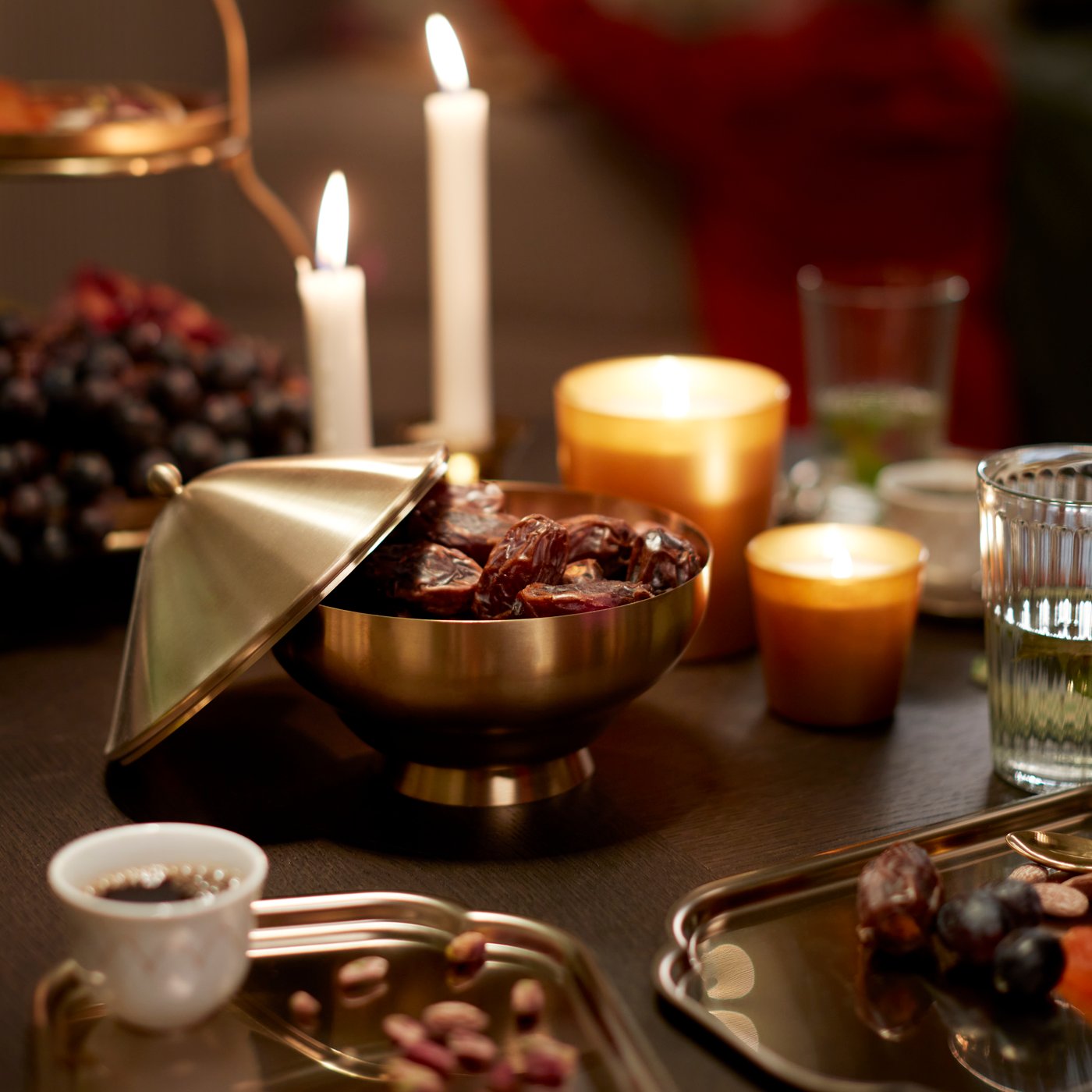 A gold-coloured GOKVÄLLÅ serving bowl filled with dates; next to some GOKVÄLLÅ side plates and a GOKVÄLLÅ tealight holder.