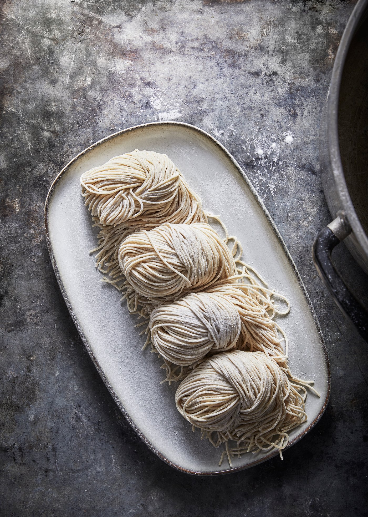 A GLADELIG plate in grey placed on a grey work surface, and holding four balls of noodles on it.