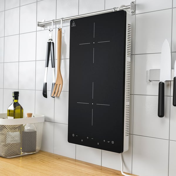 Piano cottura a induzione portatile TILLREDA bianco a 2 zone, appeso verticalmente alla parete piastrellata di una cucina.