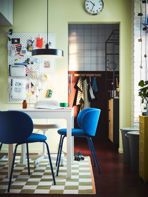 A dining area with a wall-mounted pegboard and blue KRYLBO chairs by an EKEDALEN extendable table placed on a KLASSRUM rug.