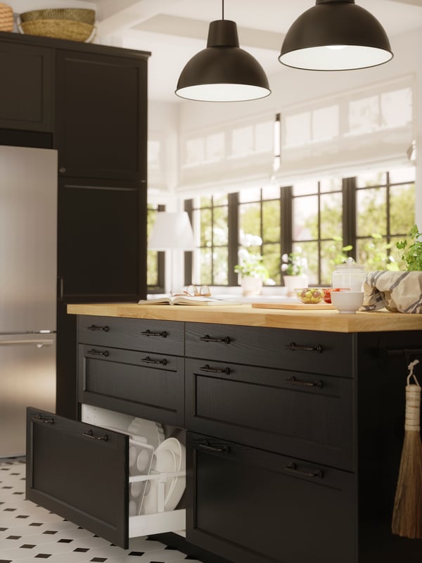 A kitchen island with LERHYTTAN black-stained fronts has a drawer that has been pulled out, showing white dishes inside.