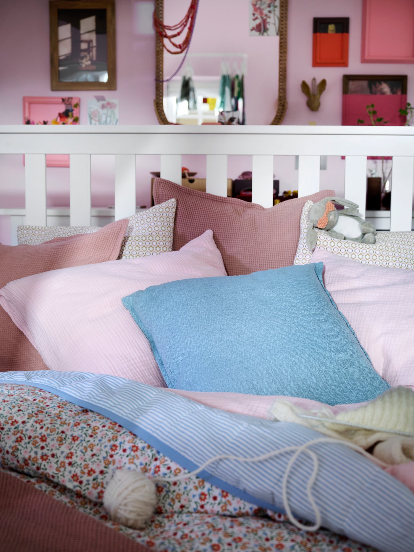 Close-up of white HEMNES bed with bedding and extra cushions in light pink, blue and a flower pattern.