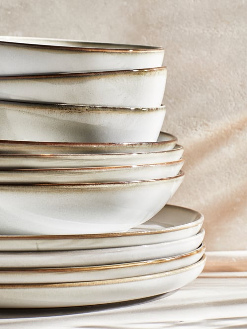 A piled set of stoneware bowls and plates on a white countertop with beige background.