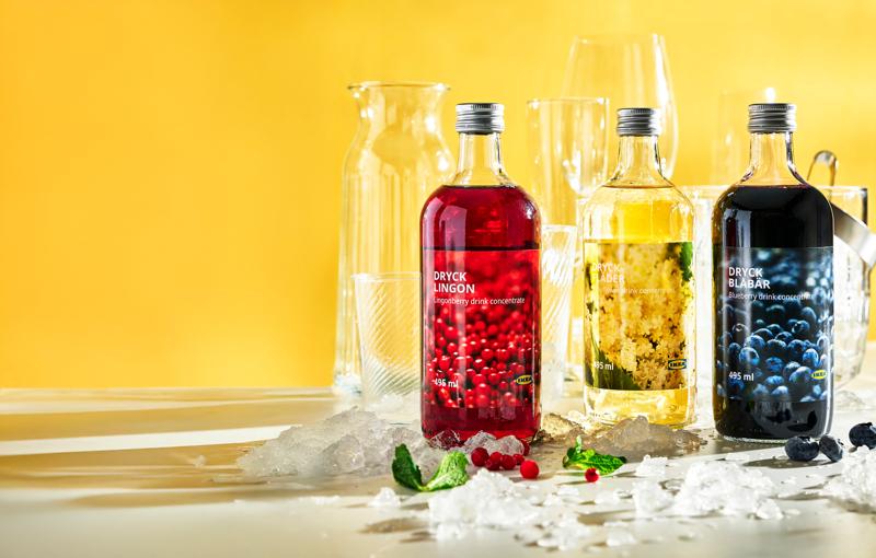 3 bouteilles de sirop avec es glaçons sur le devant et des verres en arrière plan, sur fon d jaune