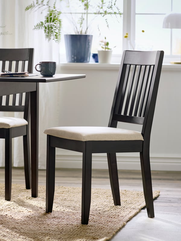 A dark brown NÄSINGE chair with light beige cushion, set beside a dining table in a bright, airy room.