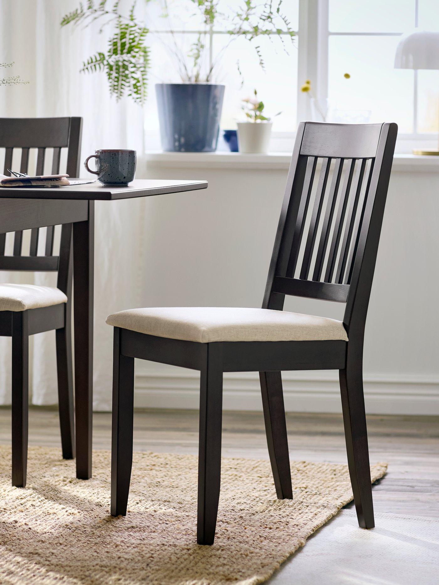 A dark brown NÄSINGE chair with light beige cushion, set beside a dining table in a bright, airy room.