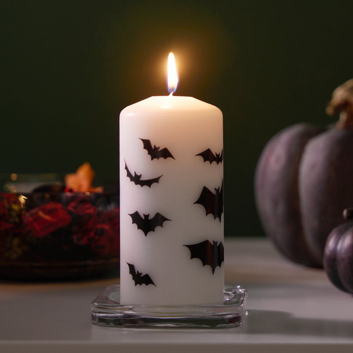 Bílá/netopýří HÖSTAGILLE neparfémovaná svíčka hoří plamenem v popředí. V pozadí jsou černé dekorace.