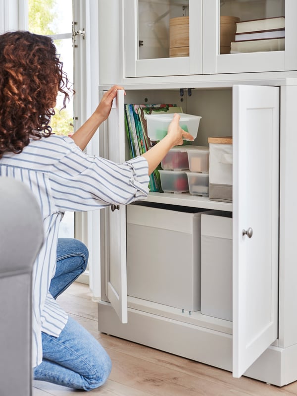 A woman places a GLIS box in a HAVSTA storage combination, the solid doors open holding two DRÖNA boxes.