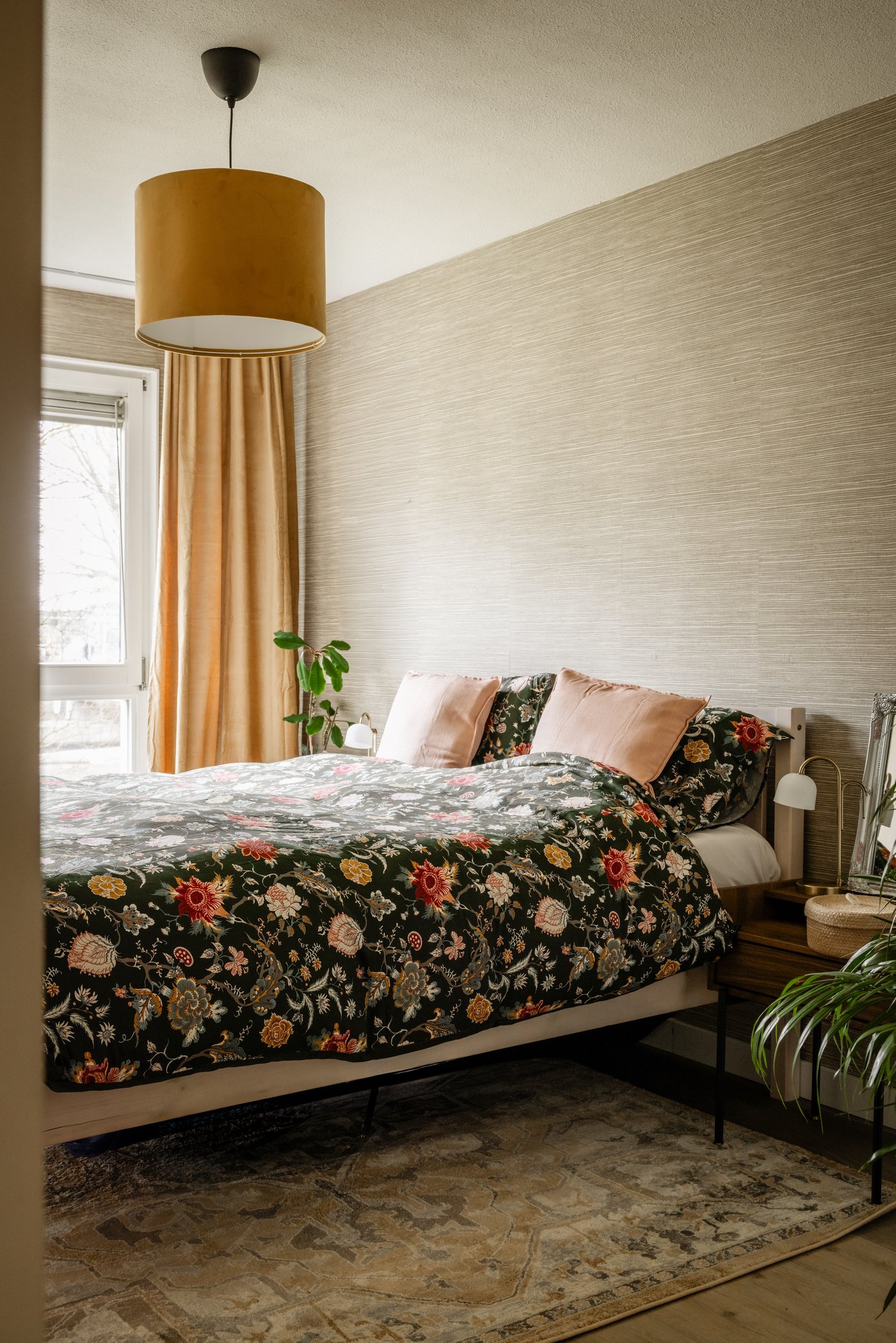 Slaapkamer met tweepersoonsbed met donkere bloemenprint. In de kamer ligt een groot JÄRNVÄG vloerkleed. Boven het bed hangt een MOLNSKIKT / SUNNEBY hanglmap in donkergeel fluweel.