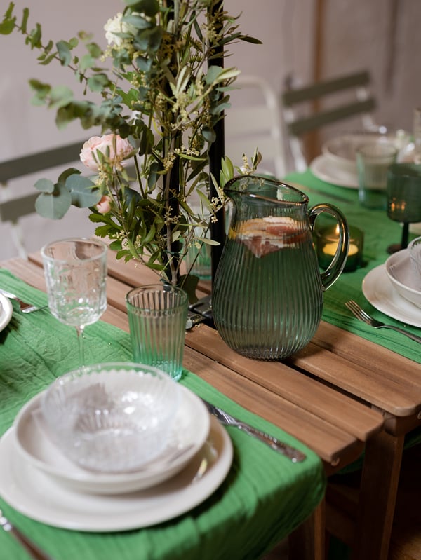 Close-up of a midsummer table setting with green tablecloth, green glasses and white plates.