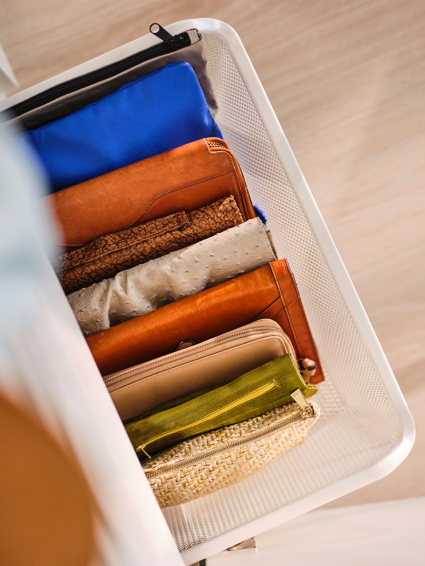Close-up taken from above a KOMPLEMENT mesh basket full of small purses and bags in neat order.