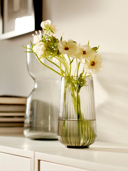 Sideboard mit einer GRADVIS und einer OMTÄNKSAM Vase auf einer EKET Schrankkombination mit Beinen. Im Hintergrund ist ein Stapel Bücher zu sehen.