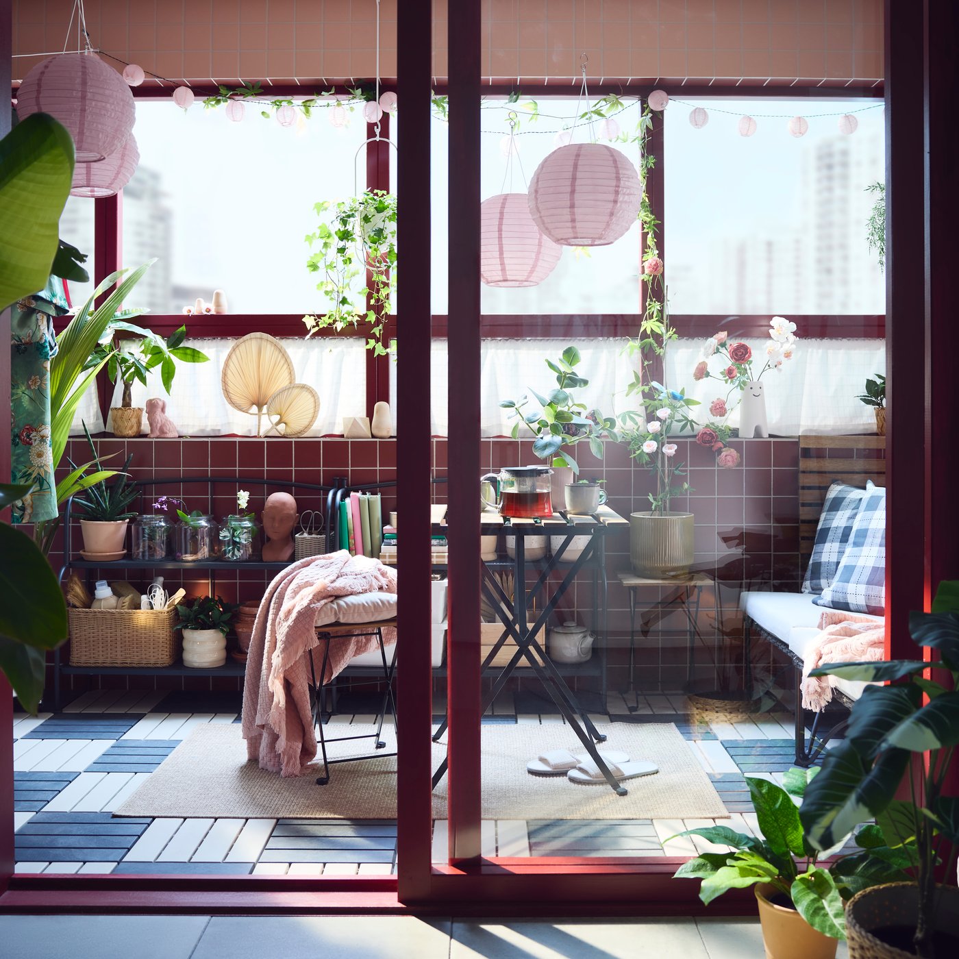Небольшой балкон с растениями и местом для сидения, освещённый солнцем и розовыми подвесными лампами на солнечных батареях.