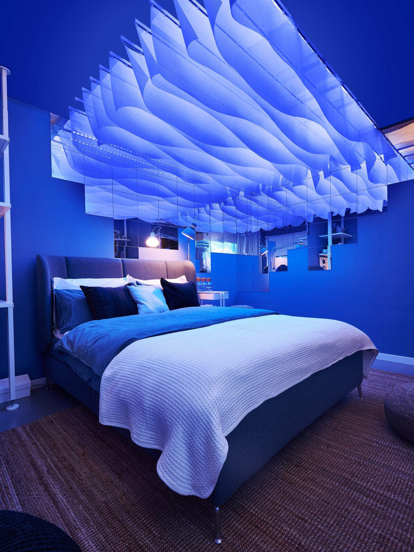 A view of a bed in a room with a blue lighting. There are hanging cut curtains above the bed creating calm atmosphere.