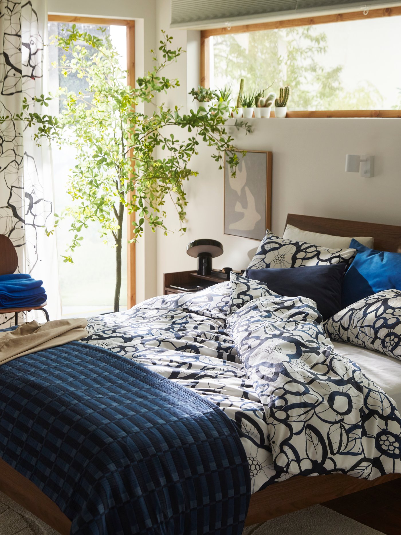 A brown bed frame with white black/blue HÄRLIR duvet cover and pillowcases and a blue SKOGSKOVALL bedspread.