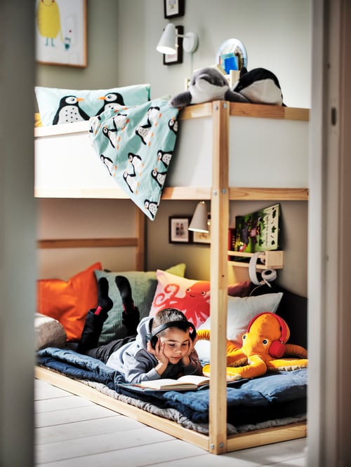 Children's room featuring a reversible bed with a high profile, under the bed is a child reading and surrounded by cushions.