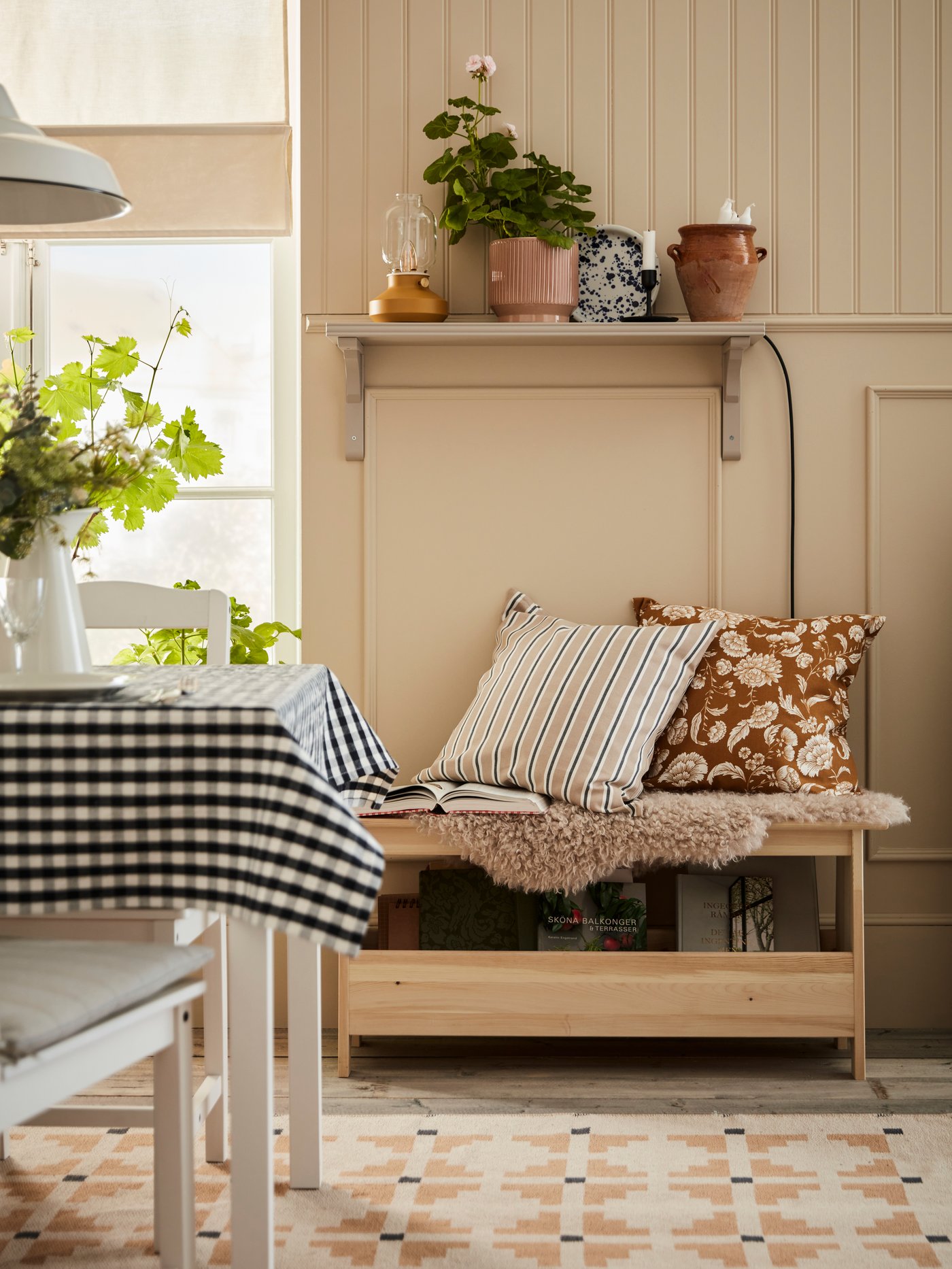 A PERJOHAN bench with storage with two cushions on it stands against a wall near a table on a SVINDINGE rug.