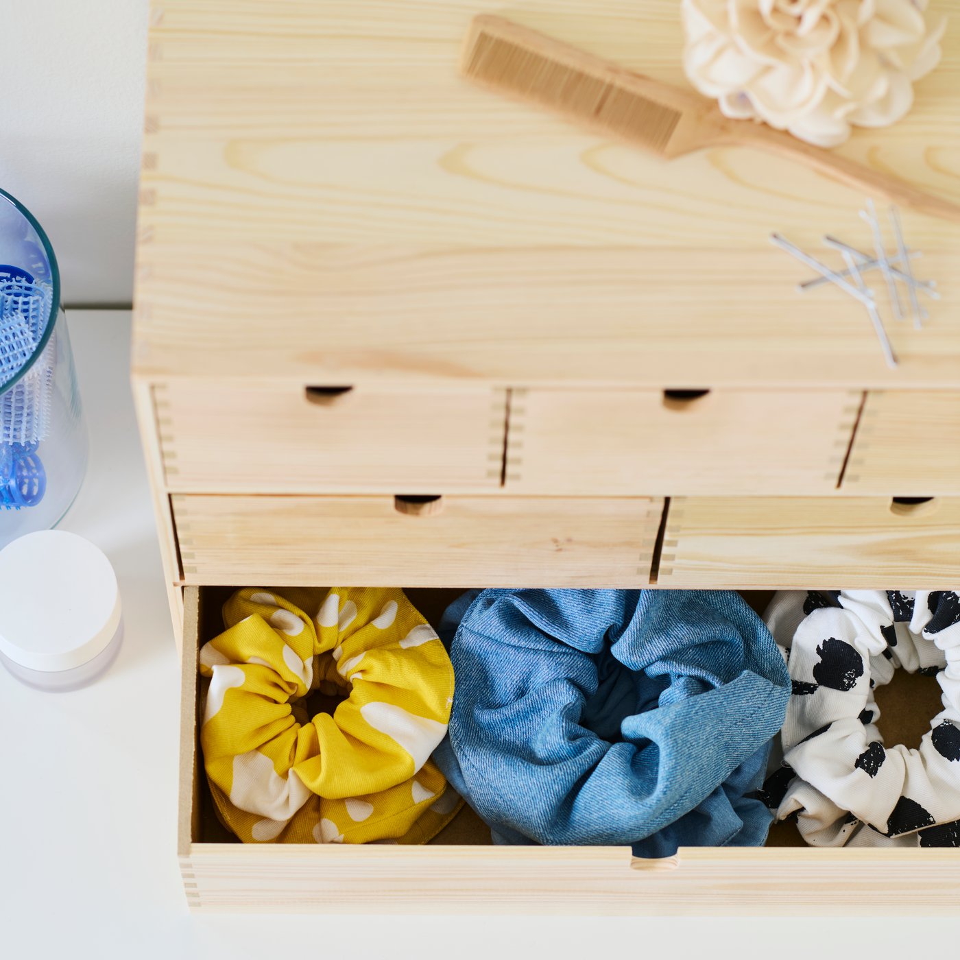 وحدة أدراج صغيرة MOPPE من الصنوبر وأدراجها السفلية مفتوحة وبها ثلاثة صفوف من ربطات شعر بألوان مختلفة.  