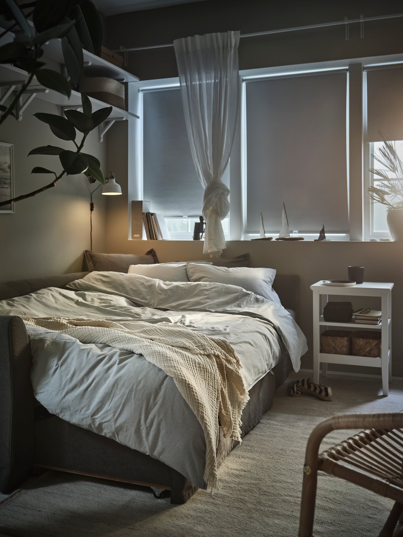 Dormitorio con una funda nórdica azul BERGPALM y 2 fundas de almohada colocadas en un sofá cama esquinero HOLMSUND junto a una manta VALLKRASSING.
