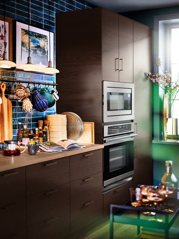 Una cocina con alacenas SEKTION, una barra SÄLJAN en laminado efecto roble, lámparas de techo TÄLLBYN y artículos de cocina colgados.