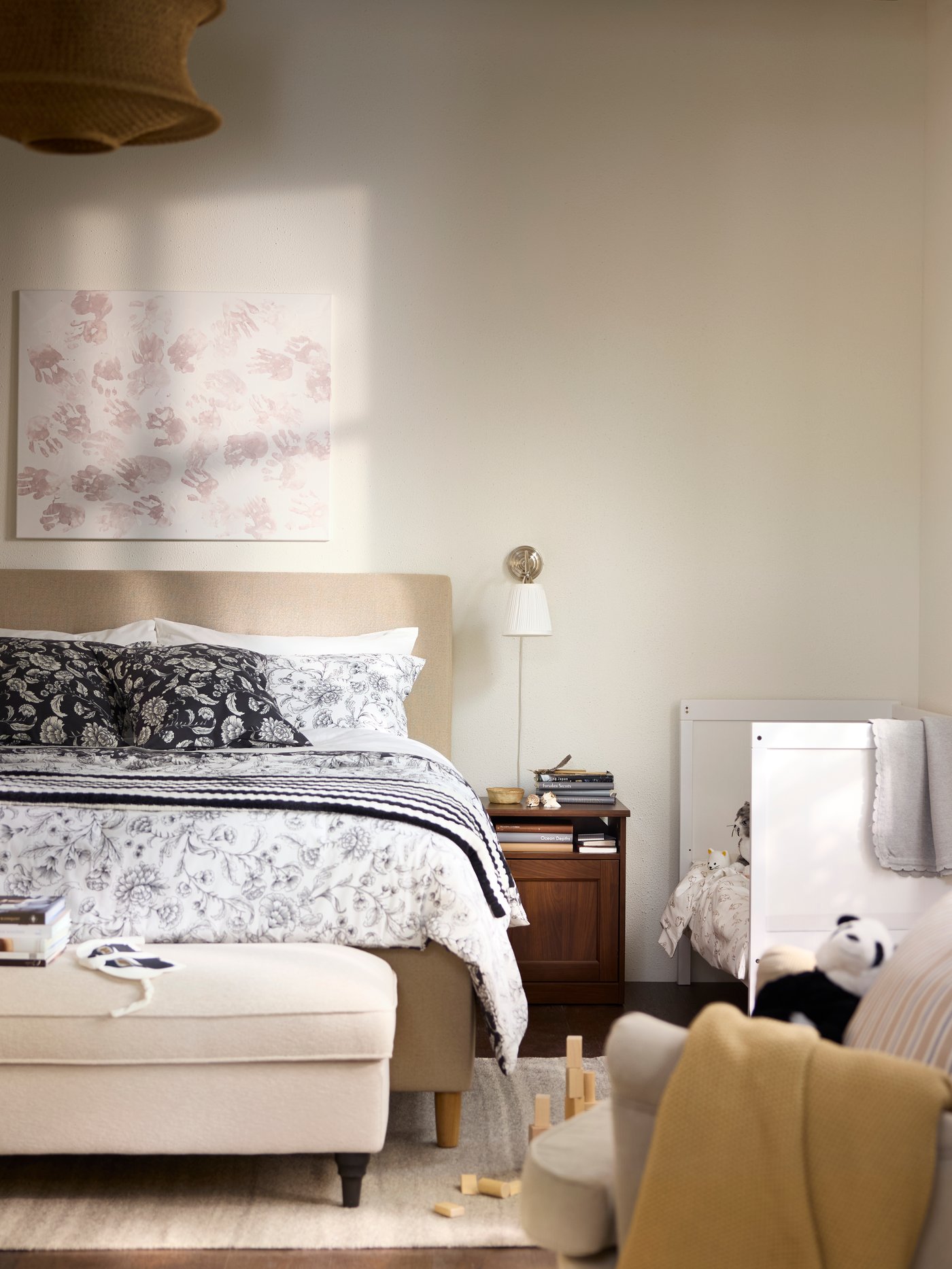 Bedroom in beige and white with a children’s bed next to the grown-up’s bed, and an armchair in the foreground.
