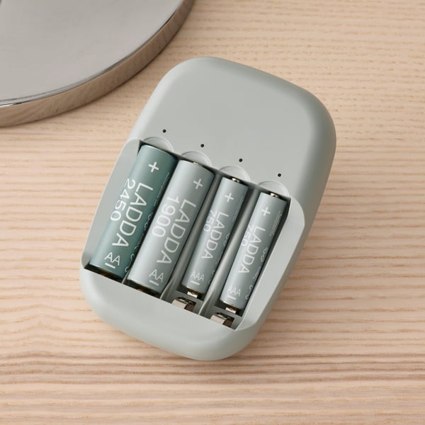 Four LADDA rechargeable batteries in a STENKOL battery charger plugged into a socket on a white wall.