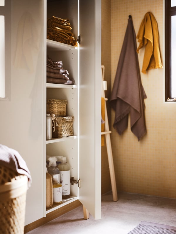 A bathroom with two high-gloss white GODMORGON high cabinets with an open door with towels, boxes and products inside.