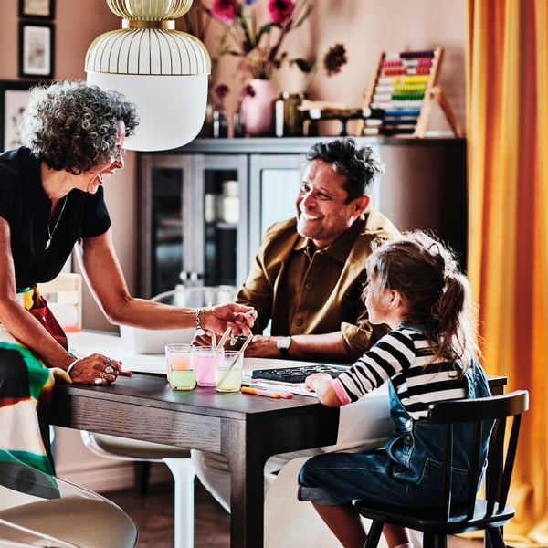 Twee volwassenen en een kind zitten aan een donkerbruine EKEDALEN uittrekbare tafel. Het kind zit op een zwarte AGAM kinderstoel.