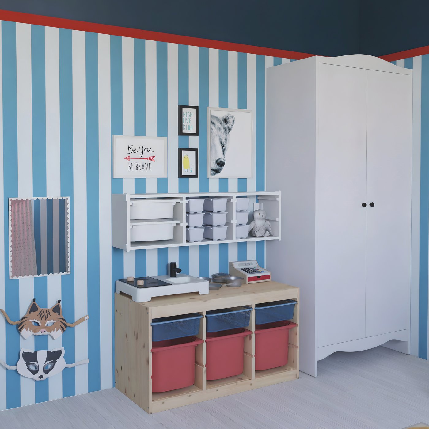 Una combinación de suelo y pared de TROFAST almacenaje en pino y blanco con cajas de color rojo, azul y blanco. También hay un armario SMÅGÖRA blanco. En la pared hay un collage de cuatro marcos, en diferentes medidas con láminas y junto a ellos un espejo.