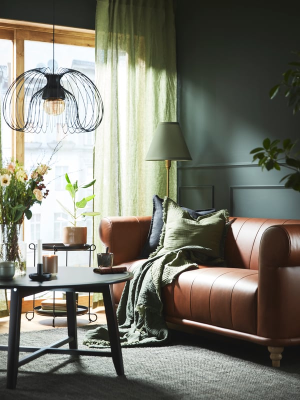 A black KRAGSTA coffee table stands under a KALLFRONT/HEMMA pendant lamp in front of a brown leather VISKAFORS 2-seat sofa.