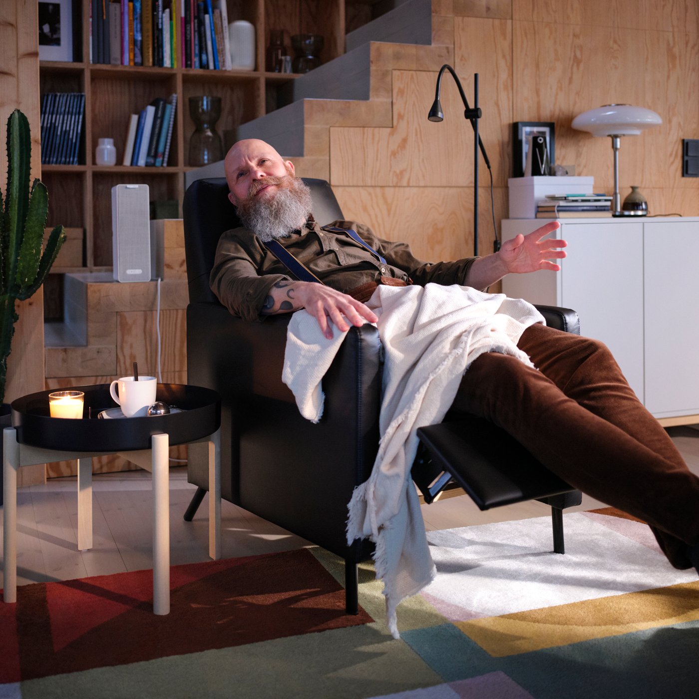 Soggiorno con un uomo seduto ad ascoltare musica su una poltrona reclinabile GISTAD nera, accanto a un tavolino con una tazza di tè.