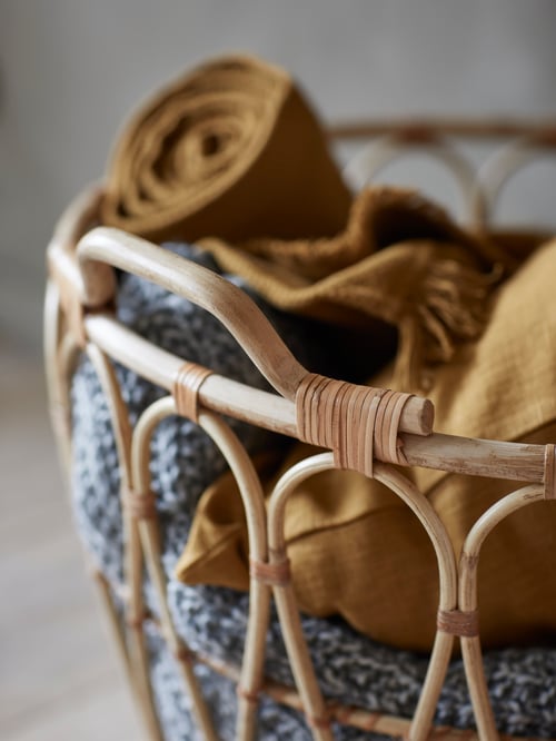 Close-up of hand-braided basket with cushion covers, throw and knitted blanket, placed in living room, on the floor.