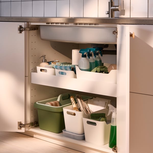 A kitchen with a white MAXIMERA low drawer, filled with UTRUSTA sink organisers filled with cleaning supplies neatly arranged.