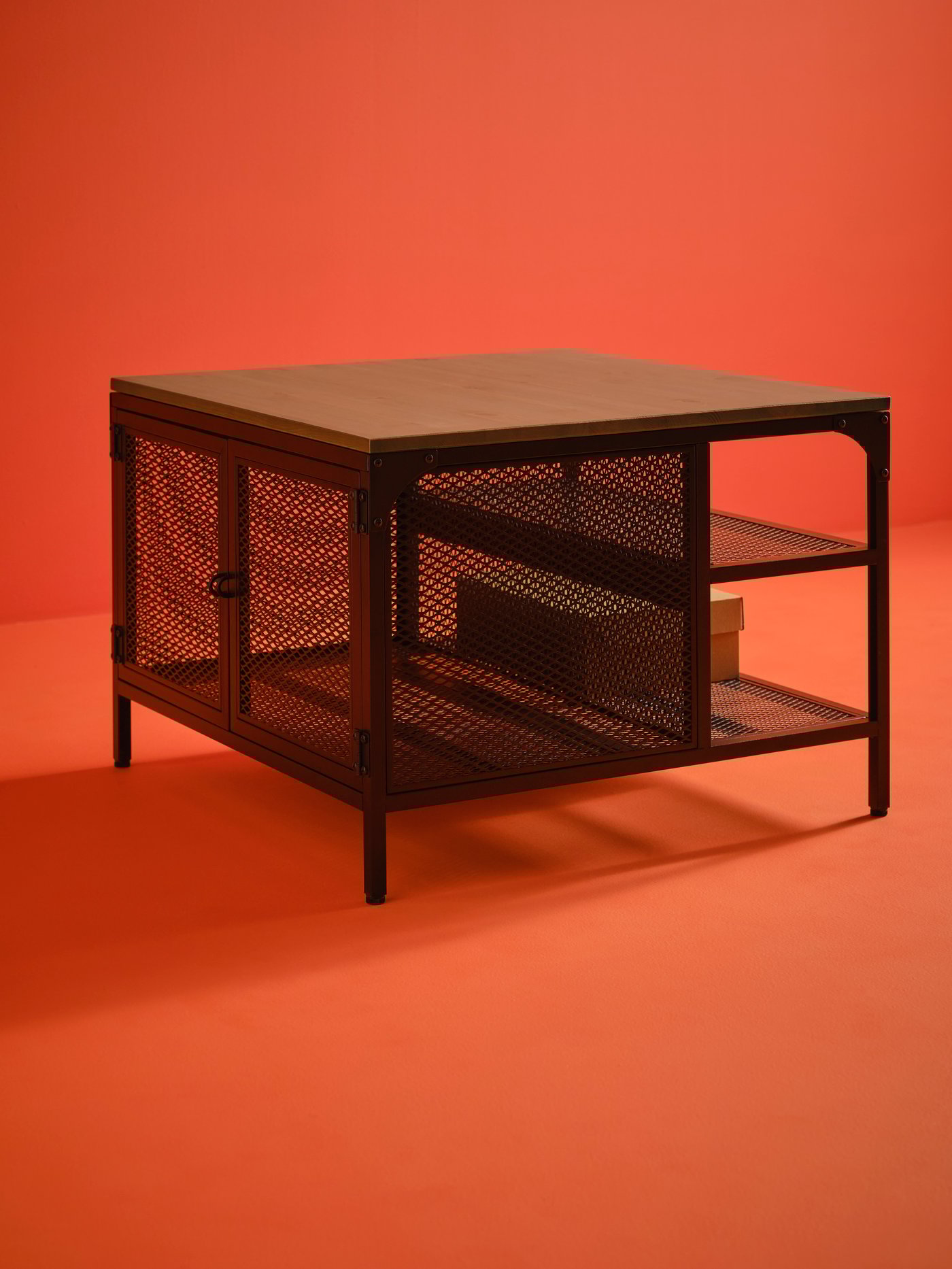 Una mesa de almacenaje FJÄLLBO negra con una encimera de madera sobre un fondo naranja.