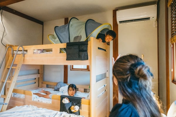 二段ベッドで遊ぶ二人の子供を見ている人物の後ろ姿