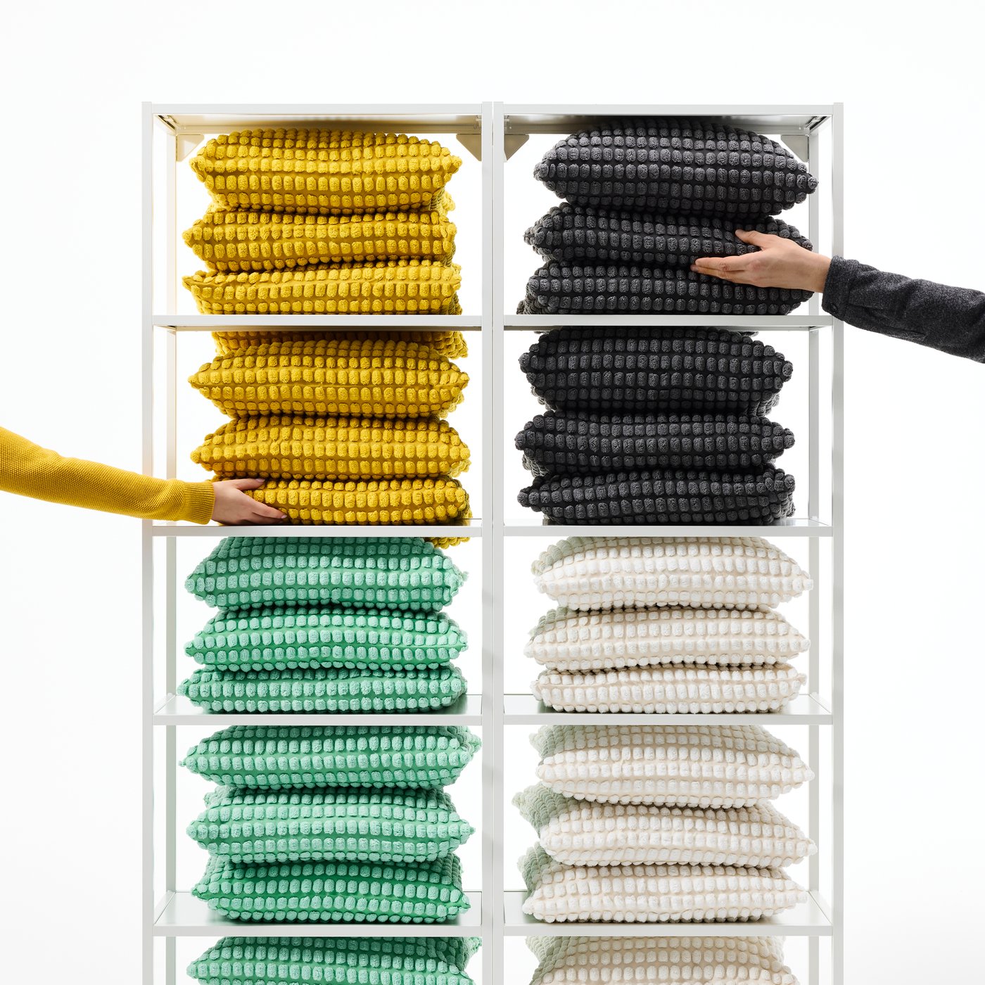 Two arms reach for cushions with SVARPOPPEL cushion covers in yellow, anthracite, light green and off-white.