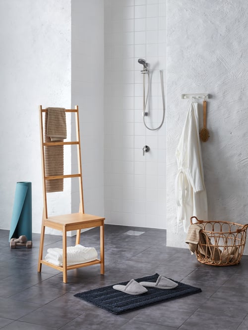 A riser rail with hand shower, and a towel rack with bath towels on the wall, and a towel rack chair, slippers, and basket.