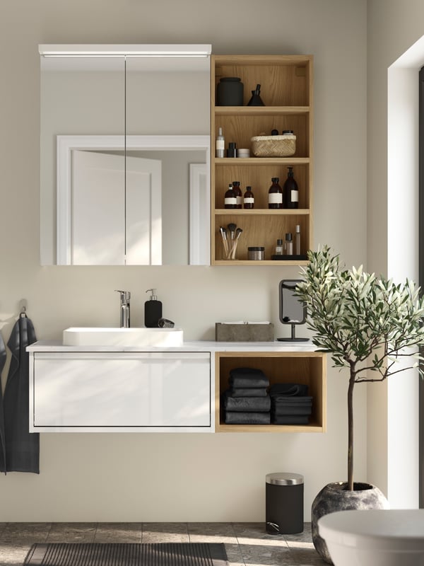 An ÄNGSJÖN vanity sink with a white high-gloss drawer and an open shelf in oak effect has a white mirror cabinet above it.