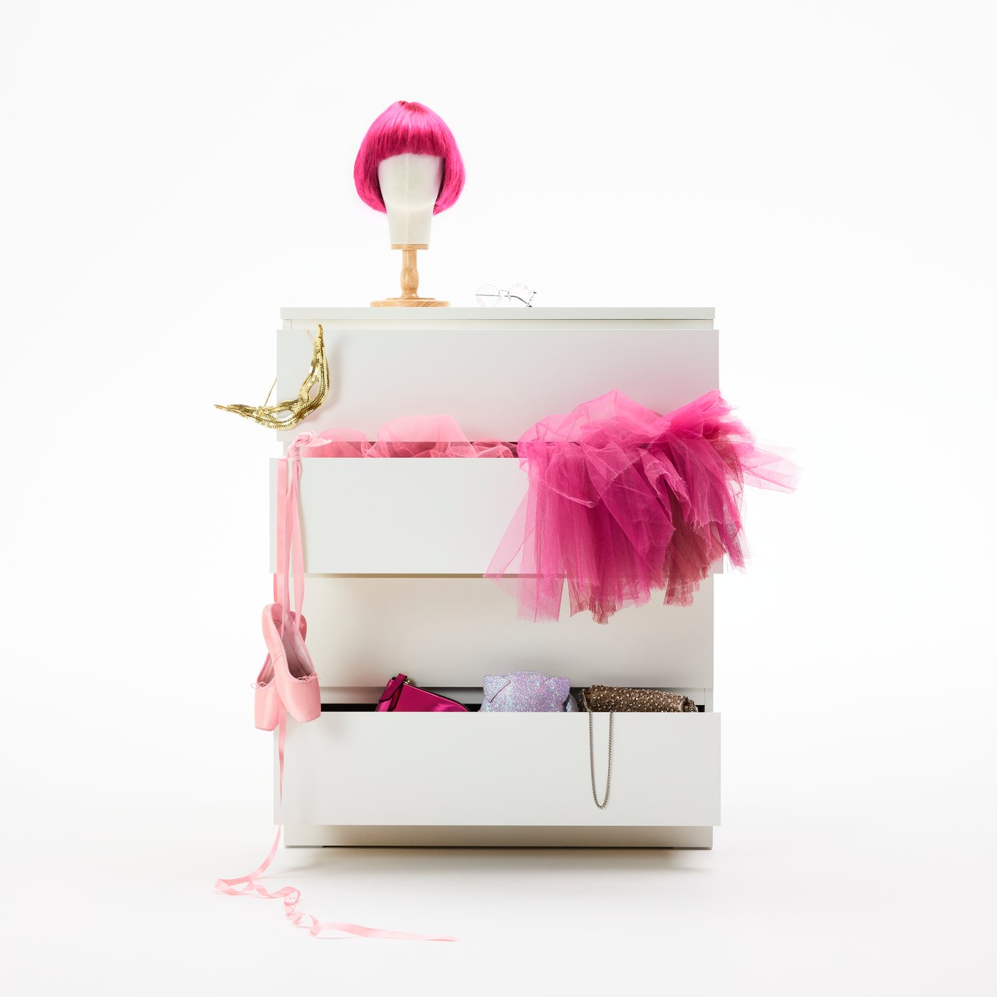 A white MALM chest of 4 drawers. The drawers are open, showing a pink tutu, ballerina shoes and a gold masquerade mask.
