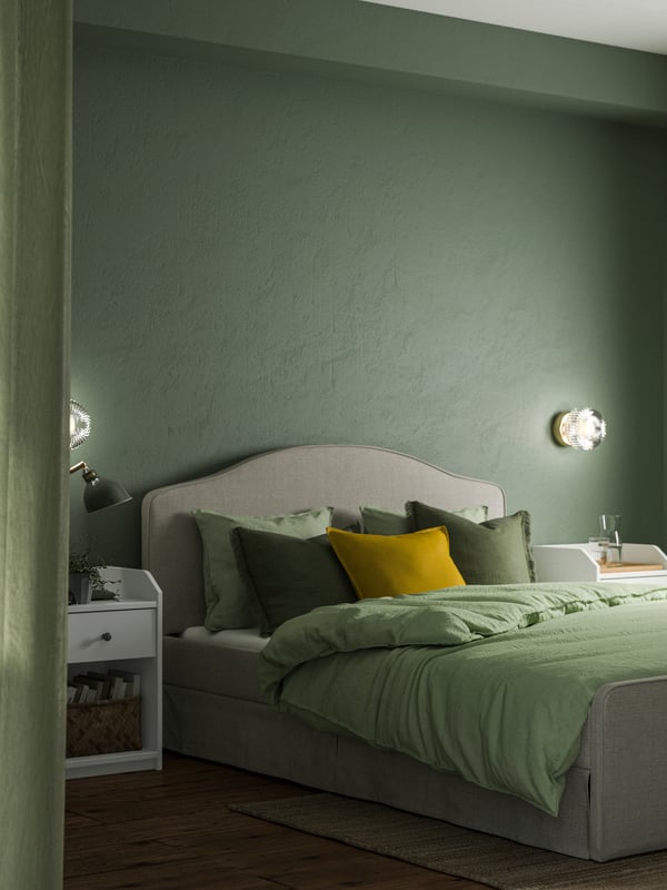 A bedroom with soft green walls and RAMNEFJÄLL upholstered bed with green bedding and lots of cushions.