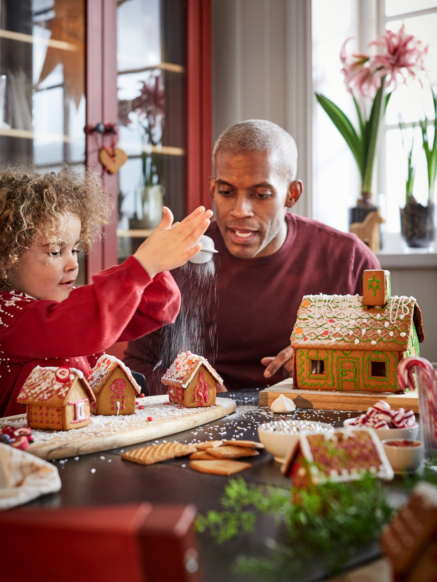 En vuxen och ett barn sitter vid ett bord och dekorerar pepparkakshus.