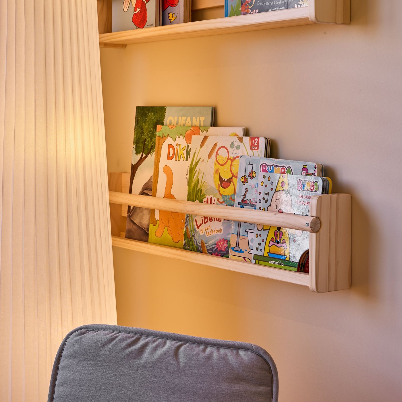 Houten wandrek met kinderboeken, zichtbaar in een rustige leeshoek met gordijnen en stoel in een warme kinderkamer.